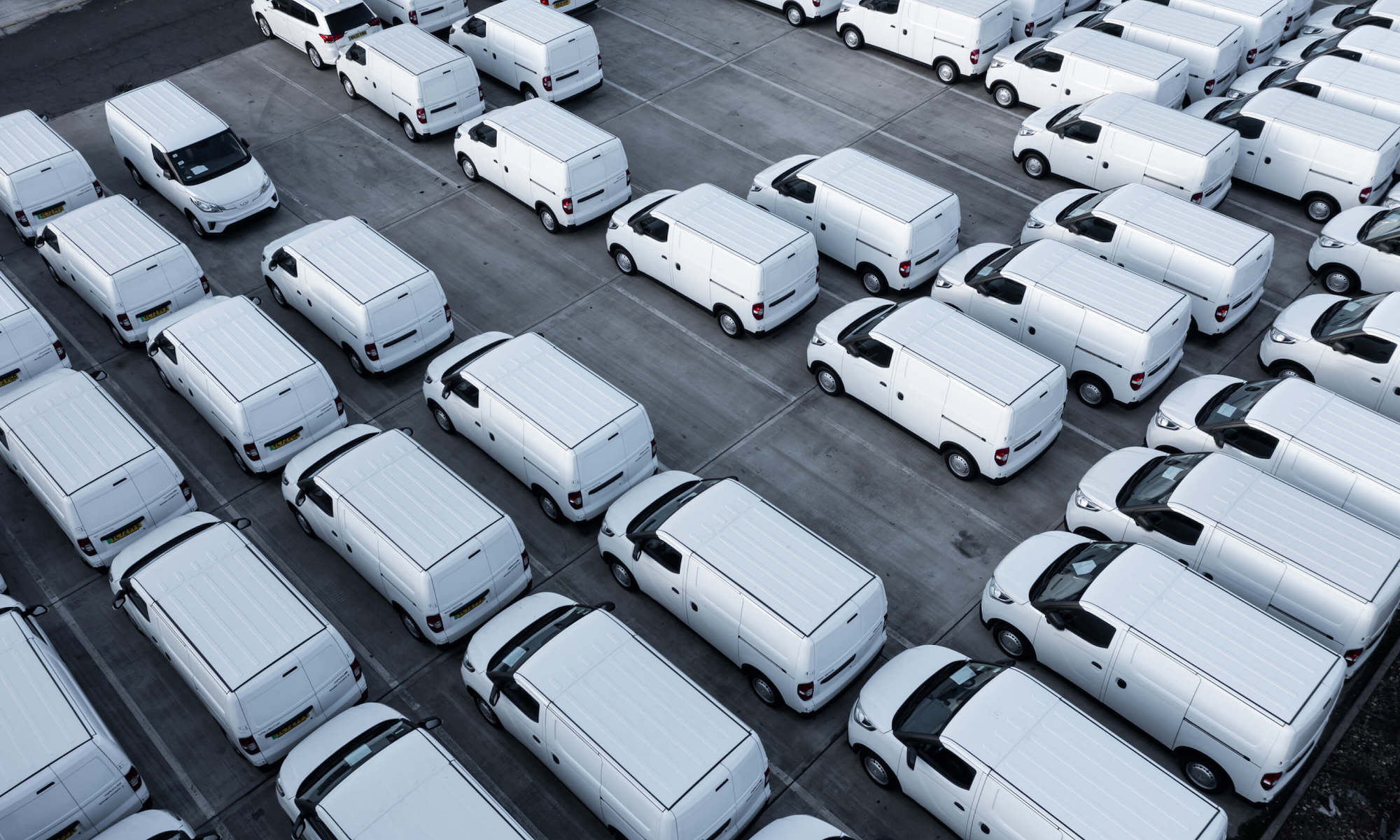 Aerial view of numerous white vans parked neatly in a large parking lot.