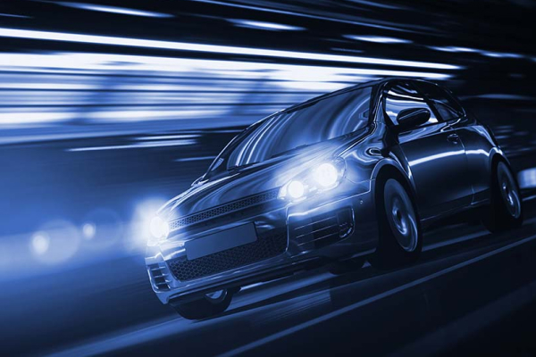 Sleek black car speeding on a road with a motion blur effect, headlights on.