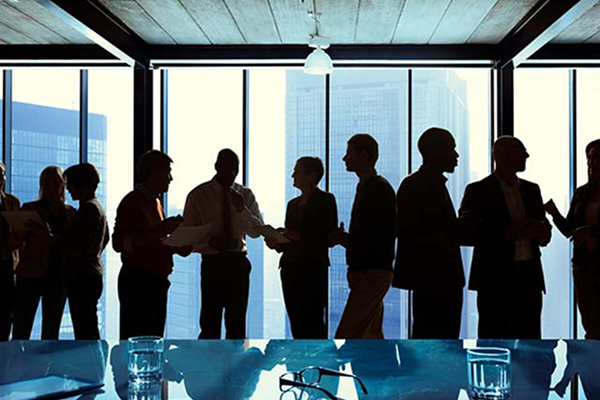 Silhouettes of people networking in a modern conference room with cityscape views through large windows.