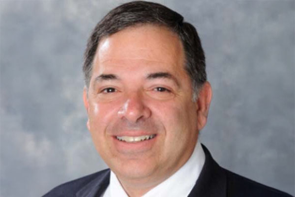 Smiling man in a suit against a gray background.