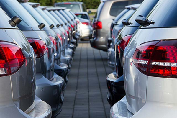 A row of parked cars seen from the rear, closely lined up on both sides of a paved path.