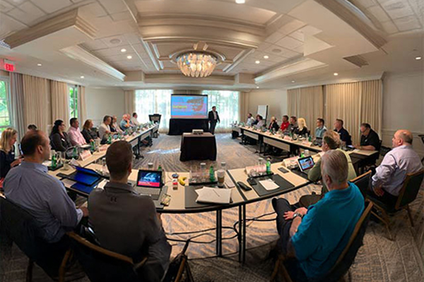 People seated around a U-shaped table in a conference room, listening to a presentation.
