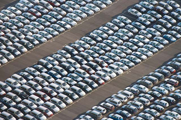 Aerial view of many white cars parked in orderly rows, filling a large outdoor lot.