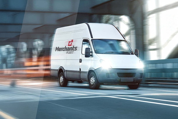 White delivery van with "Merchants Fleet" logo drives quickly on a city street, motion blur surrounding it.