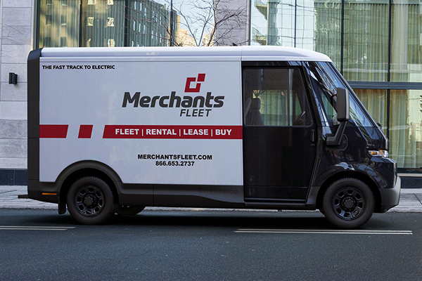 Electric van with "Merchants Fleet" branding parked on a city street beside a modern building.