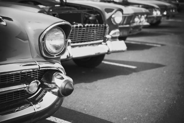 Close-up of the front of vintage cars parked in a row, shown in black and white.