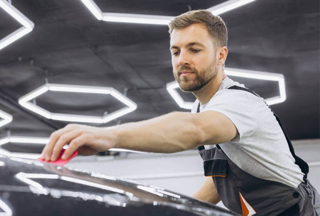 Man in overalls polishing a car under bright hexagonal lights.