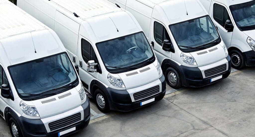 Four white delivery vans parked in a row on a concrete lot.