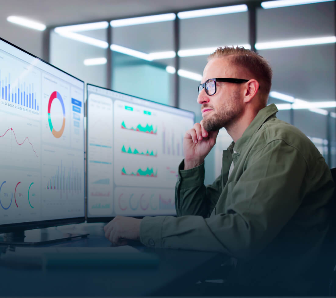 Man analyzing charts on dual monitors in a modern office.