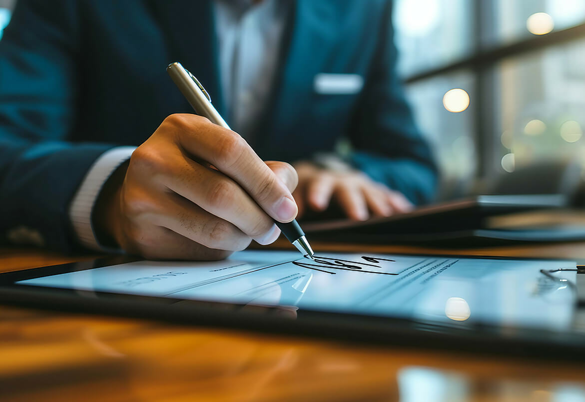 Person in a suit signing a document on a tablet with a stylus in a well-lit office environment.