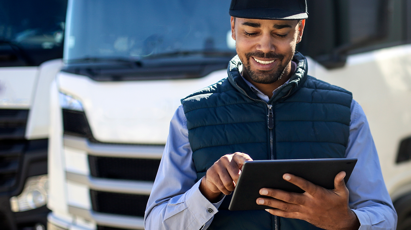 Smiling man in a cap uses a tablet in front of a white truck.