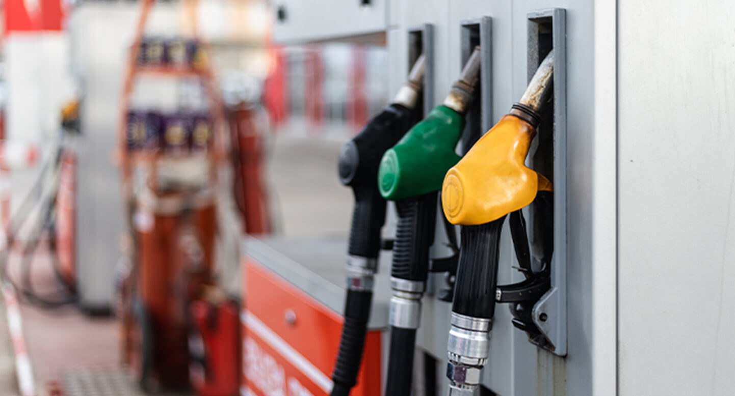 Close-up of fuel pumps at a gas station, with green, yellow, and black nozzles on a dispenser.