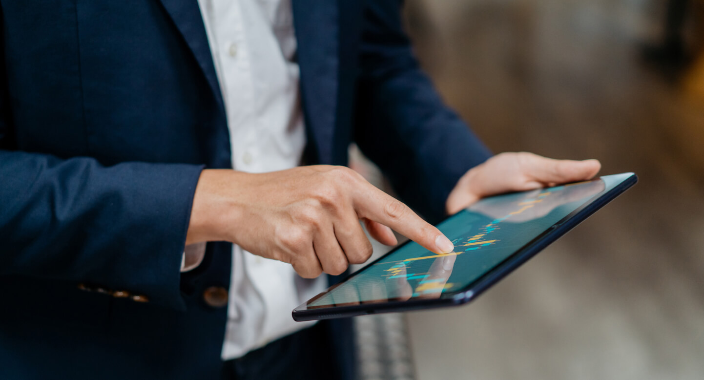 Person in a blue suit using a tablet with financial graphs on the screen.