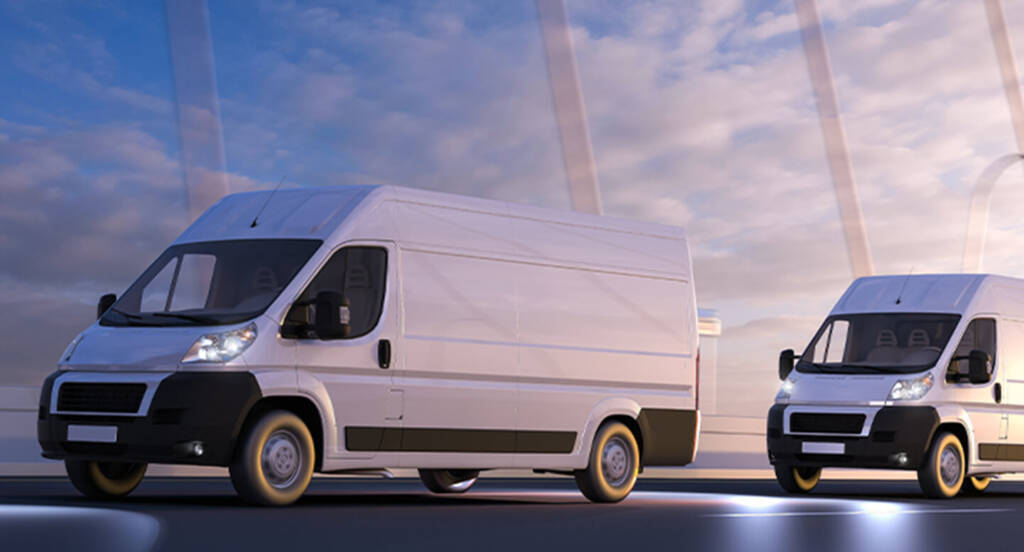 Two white delivery vans driving on a road with a cloudy sky in the background.