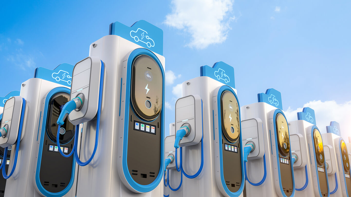 Row of electric vehicle charging stations with blue and white design against a cloudy sky.