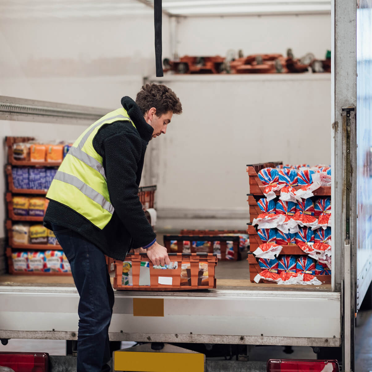 Worker in a high-visibility vest loads boxes of packaged bread into a delivery truck.